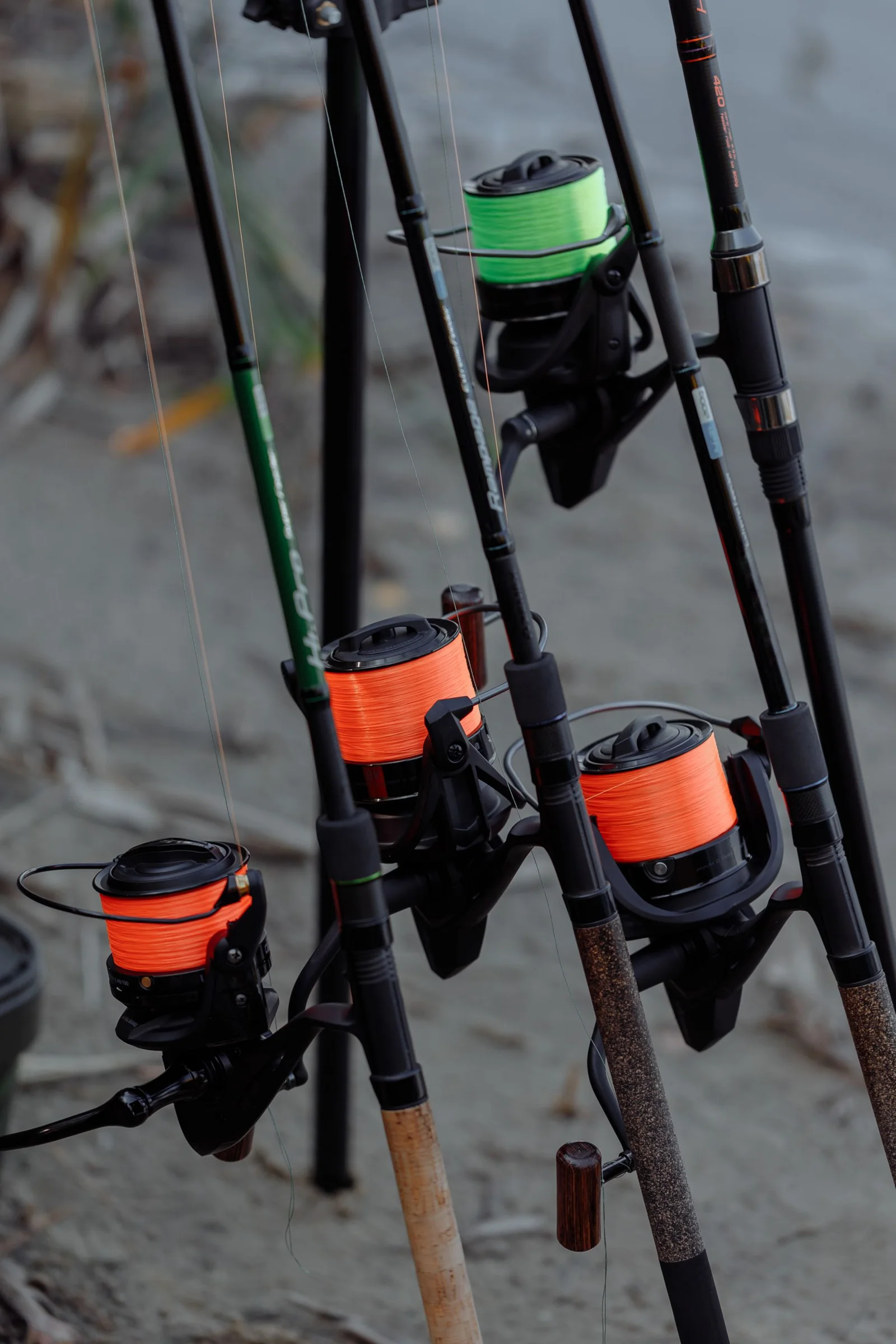 Close view of fishing rods and reels on a sandy riverbank.